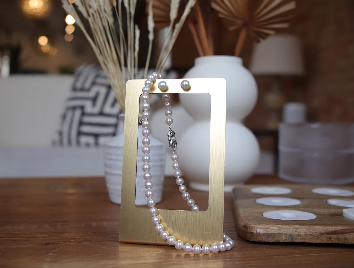 Strand of pearls and pearl stud earrings on gold jewelry stand