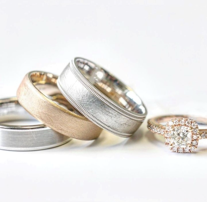 Stack of men's wedding bands next to a rose gold diamond engagement ring