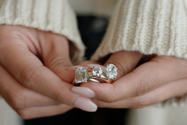 Woman holding emerald, round, and oval shaped solitaire engagement rings