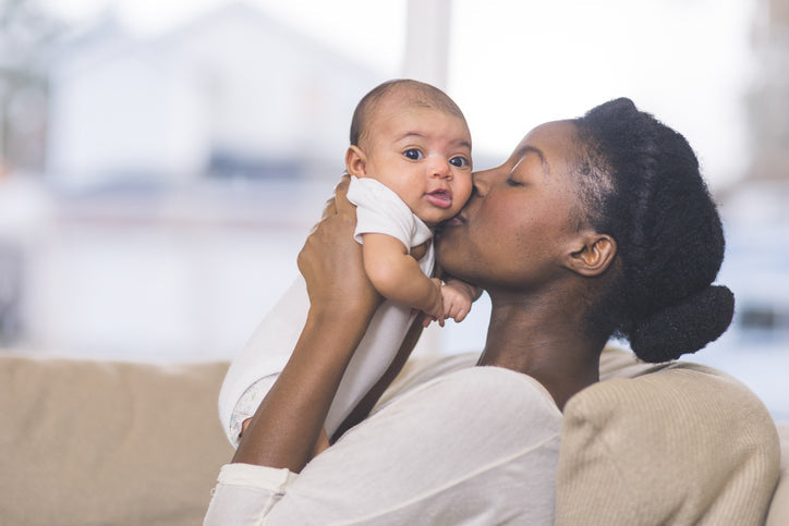 mom kissing newborn baby while sitting on tan couch