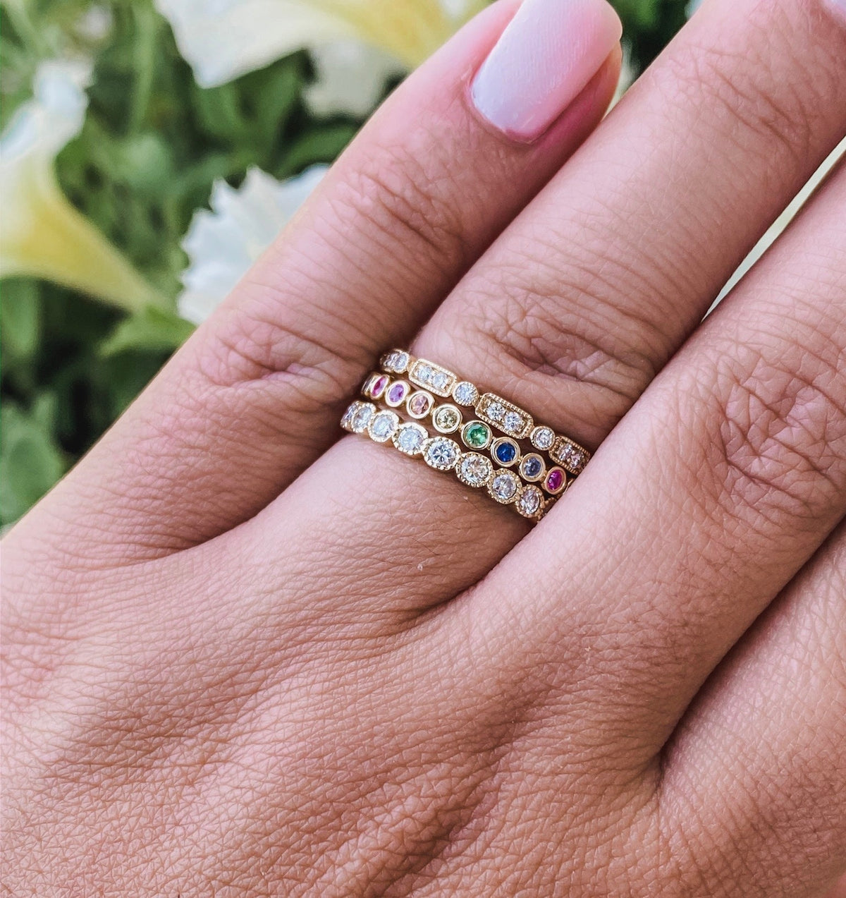 Woman wearing diamond stacking rings stacked with a rainbow sapphire band