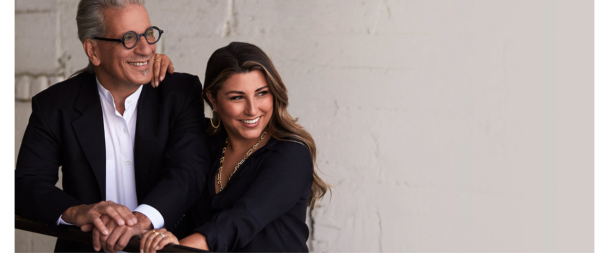 Man and woman in formal attire standing close together against a light gray wall.
